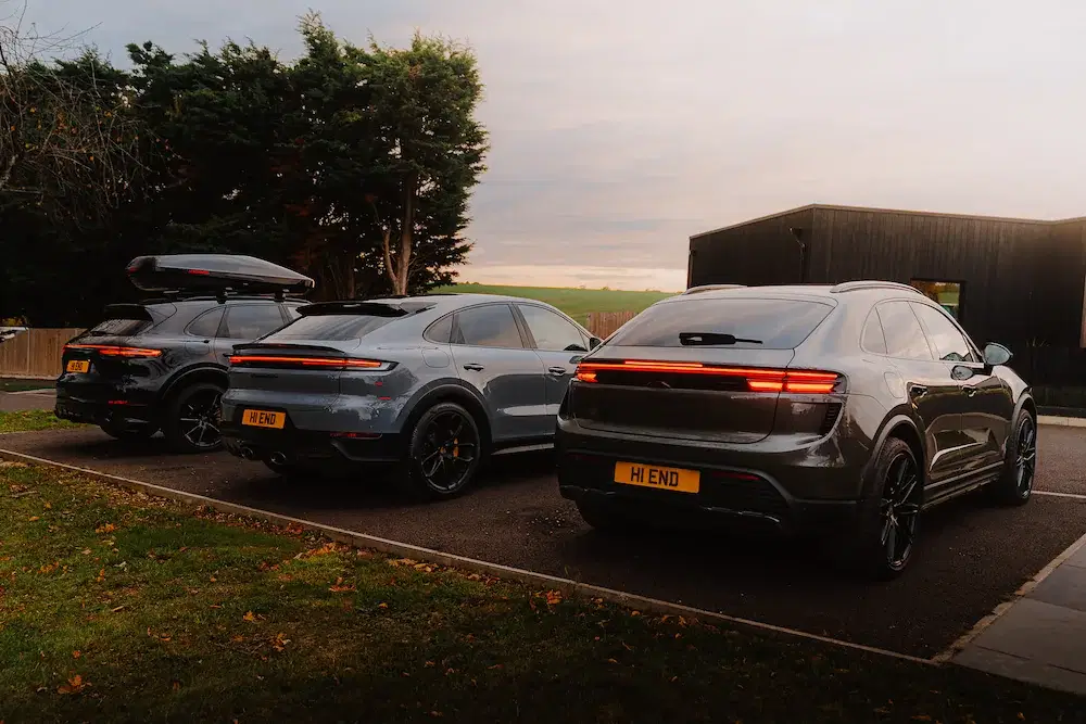 Three luxury SUVs with glowing taillights parked at sunset near a modern building and open countryside.
