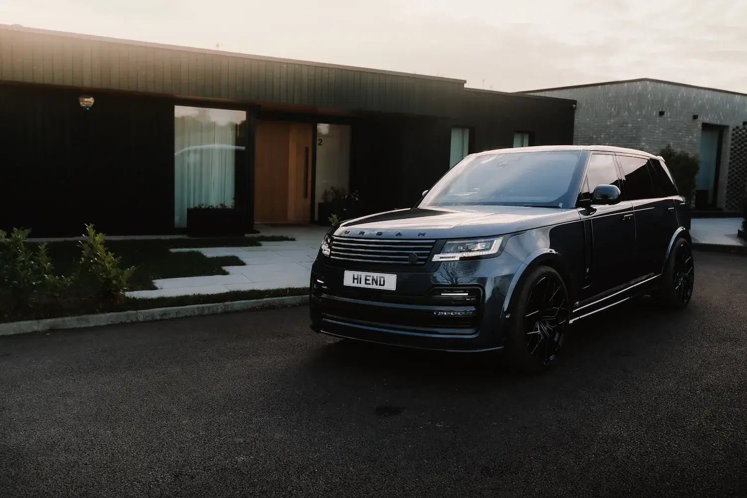 An Urban Range Rover with a “HI END” number plate parked outside a modern, minimalist home at sunset.